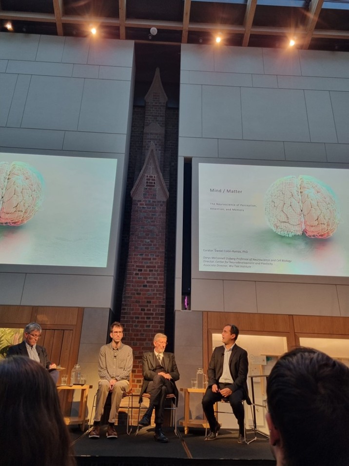 Quattro uomini su un palcoscenico moderno e scuro; alle loro spalle, proiezione di slide con immagine di Camillo Golgi