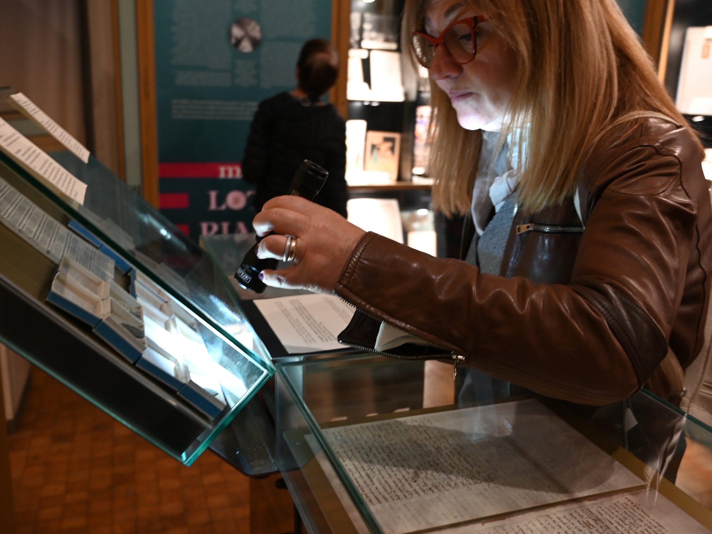 A blond woman uses a museum flashlight to look closesly at ancient coins on exhibition 